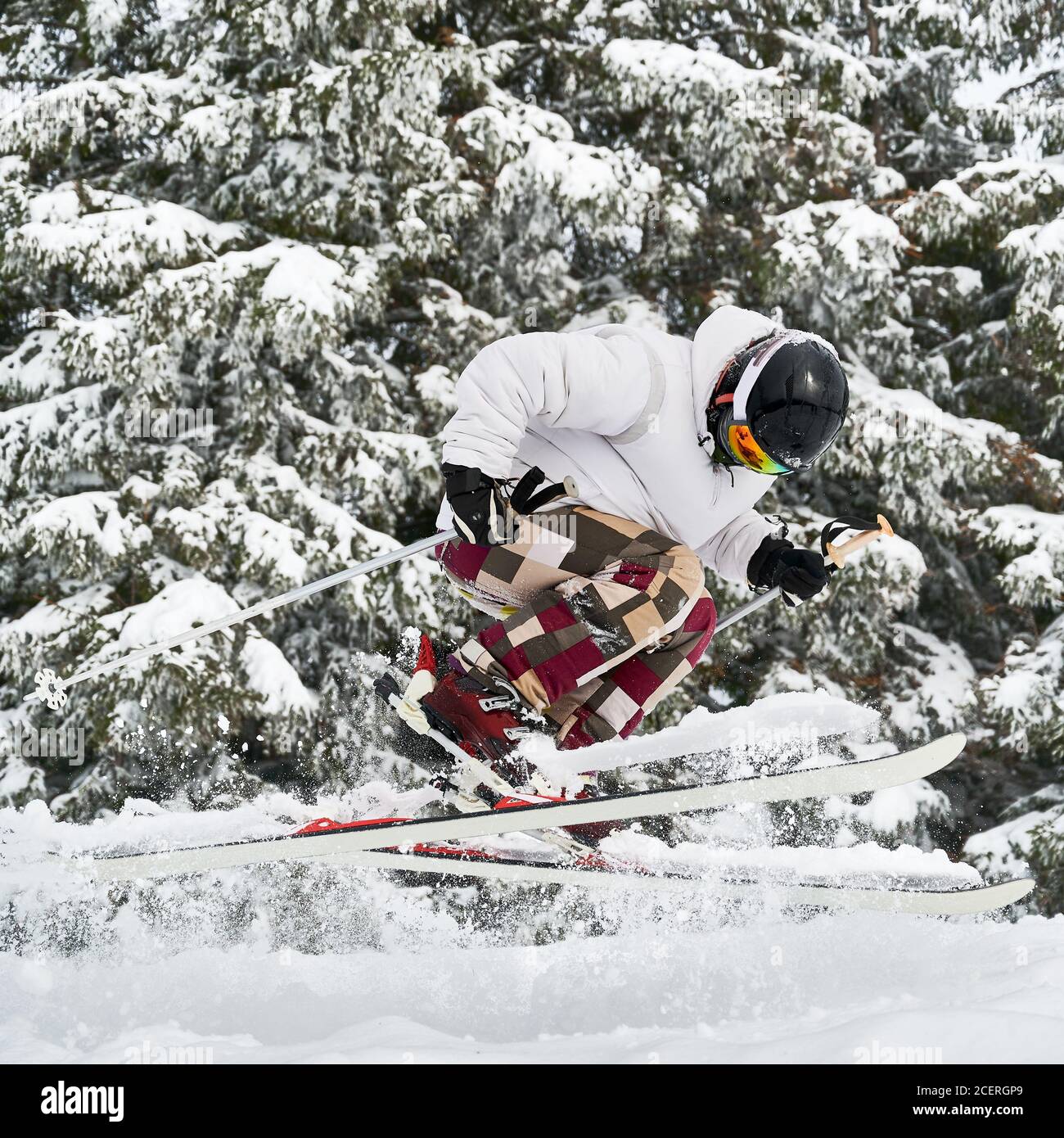 Male Skier In White Jacket And Helmet Skiing On Fresh Powder Snow With Snowy Trees On Background Man In Ski Goggles Making Jump While Sliding Down Snow Covered Slopes Concept Of Winter Sports Male Skier In White Jacket And Helmet Skiing On Fresh Powder Snow With Snowy Trees On Background Man In Ski Goggles Making Jump While Sliding Down Snow Covered Slopes Concept Of Winter Sports