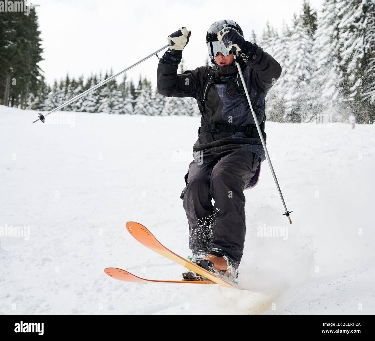 Man skier in black ski suit and goggles skiing downhill trough deep powder  snow. Young man freerider in helmet using ski poles and gliding on snow at  ski resort. Concept of skiing