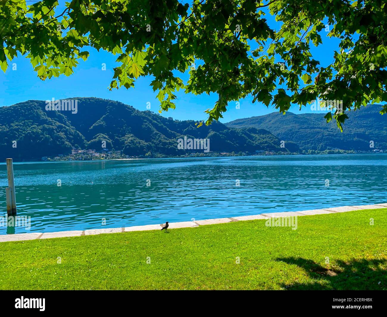 Waterfront on Alpine Lake Lugano with Mountainin a Sunny Say in Caslano, Ticino in Switzerland. Stock Photo