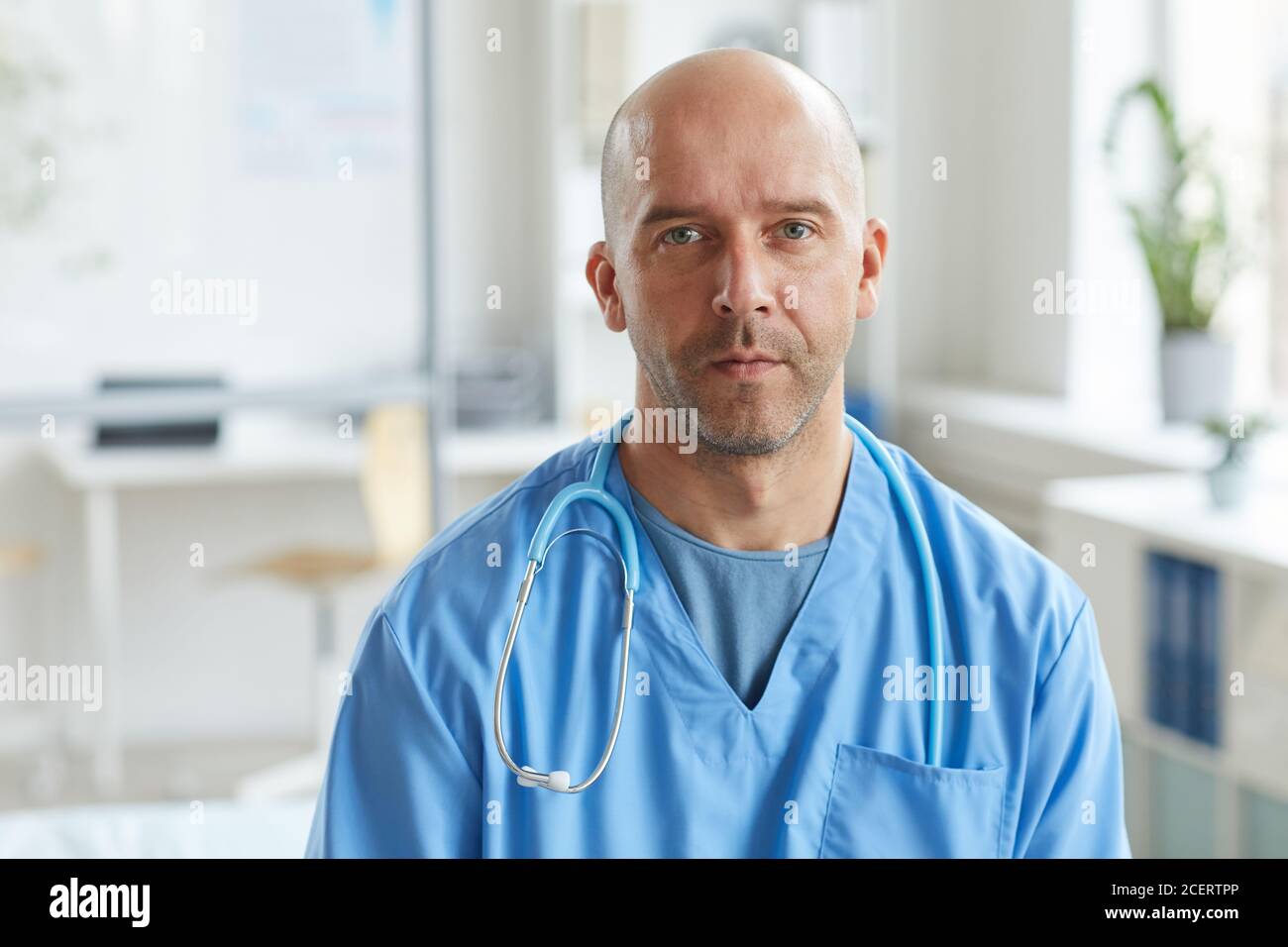 Medium close-up portrait shot of mature doctor wearing blue uniform looking at camera with serious facial expression Stock Photo