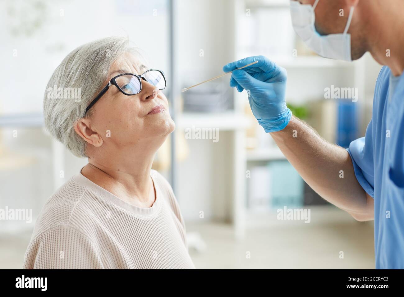 Professional medical worker wearing personal protective equipment testing senior woman for