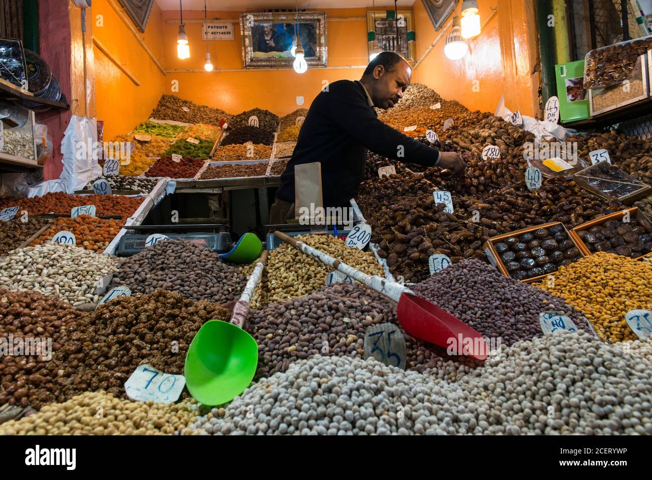 Man serving in his covered stall selling dates and nuts  in the souk inside  the Medina, Marrakesh. Stock Photo