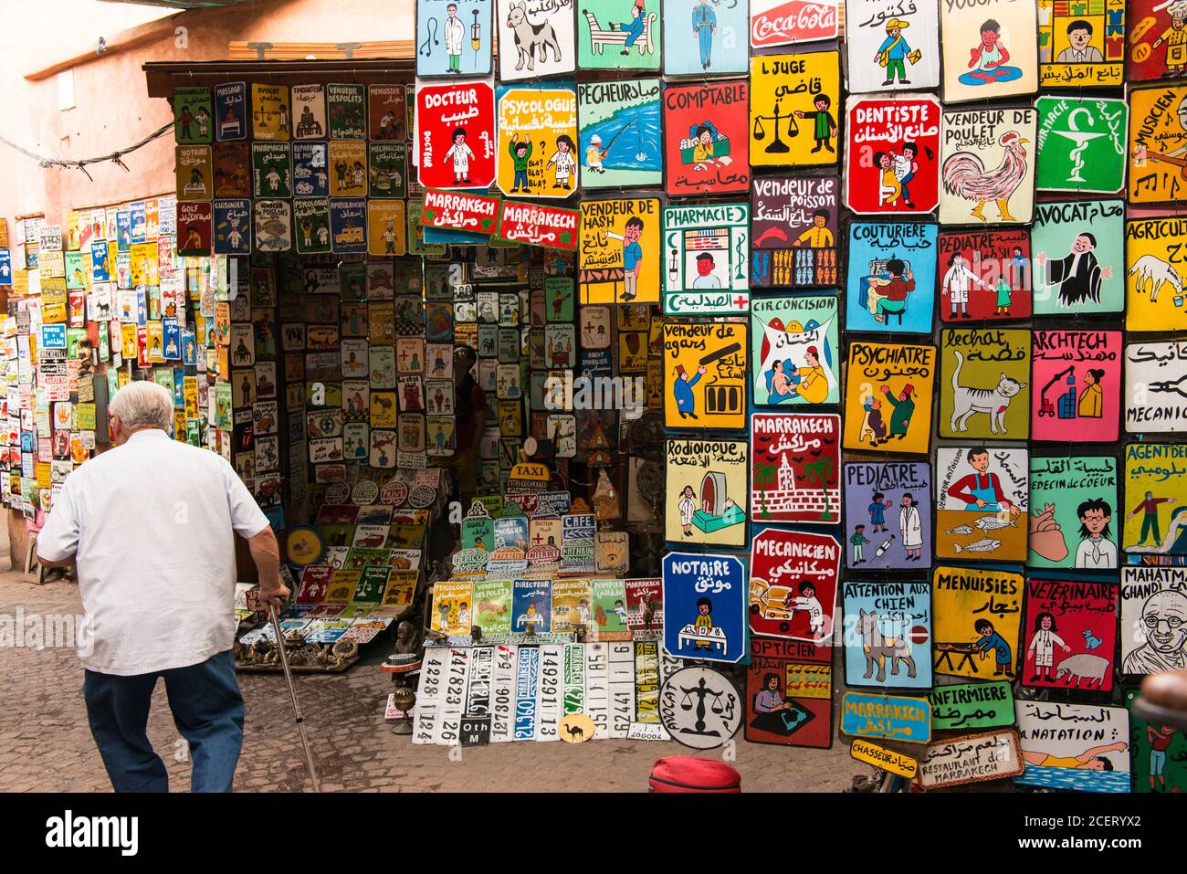 Man with walking stick walks past a stall selling hand painted signs in the souk within the Medina, Marrakesh Stock Photo