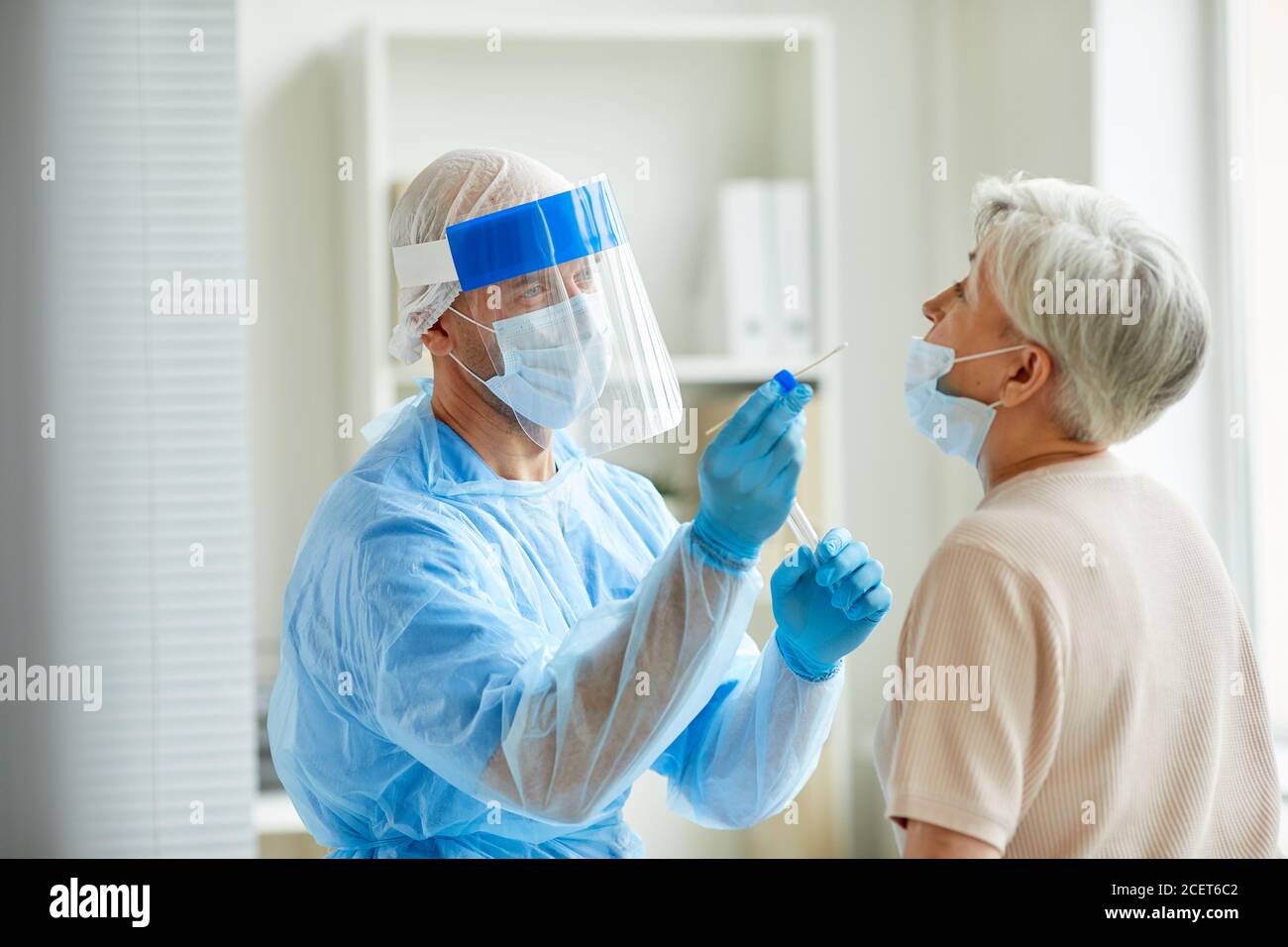 Modern laboratory worker wearing personal protective equipment testing senior woman for