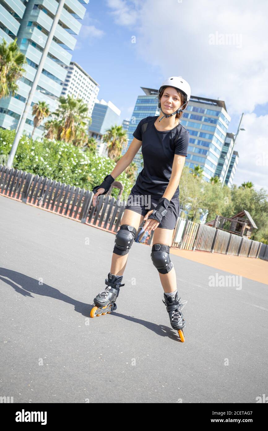 Young happy roller skater caucasian woman in the white helmet and black sporty clothes, sunny day, skatepark, urban environment. Diagonal composition. Stock Photo