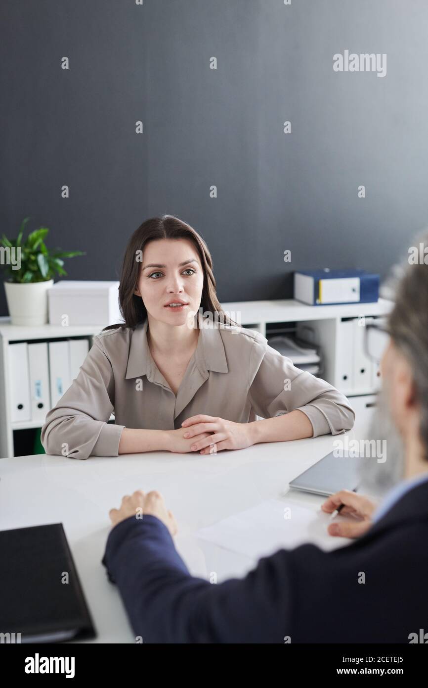 Beautiful young woman sitting in front of unrecognizable HR manager in office room having job interview Stock Photo