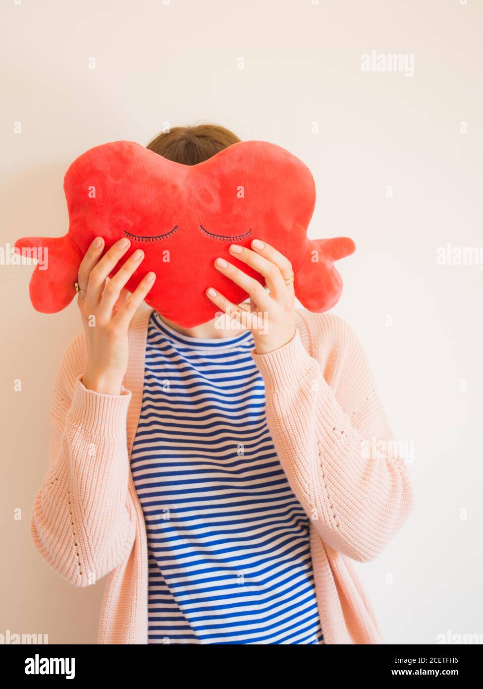 Faceless woman covering face with red heart toy Stock Photo