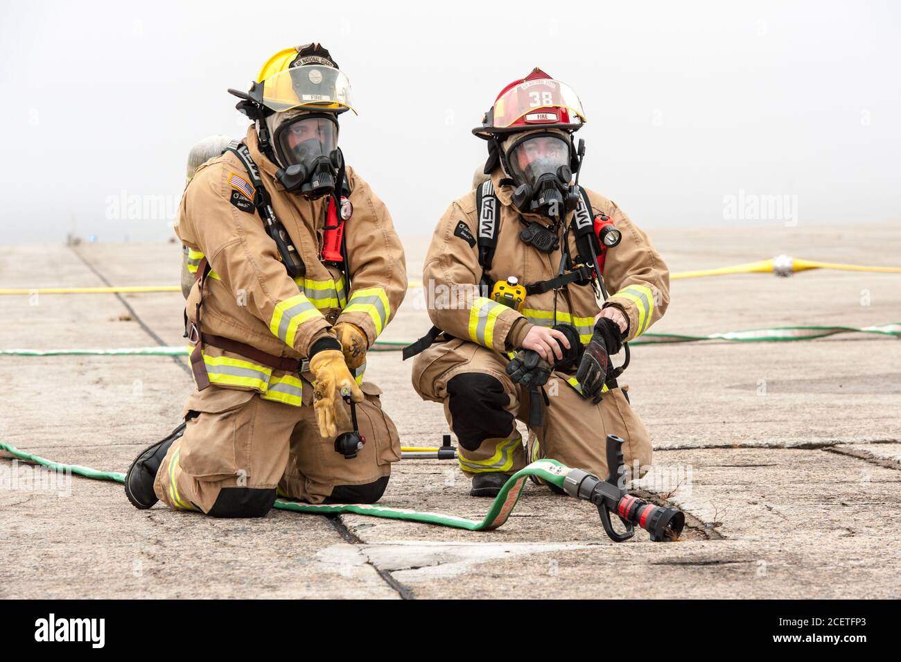 Two firefighters sitting on the tarmac while putting on their gear at