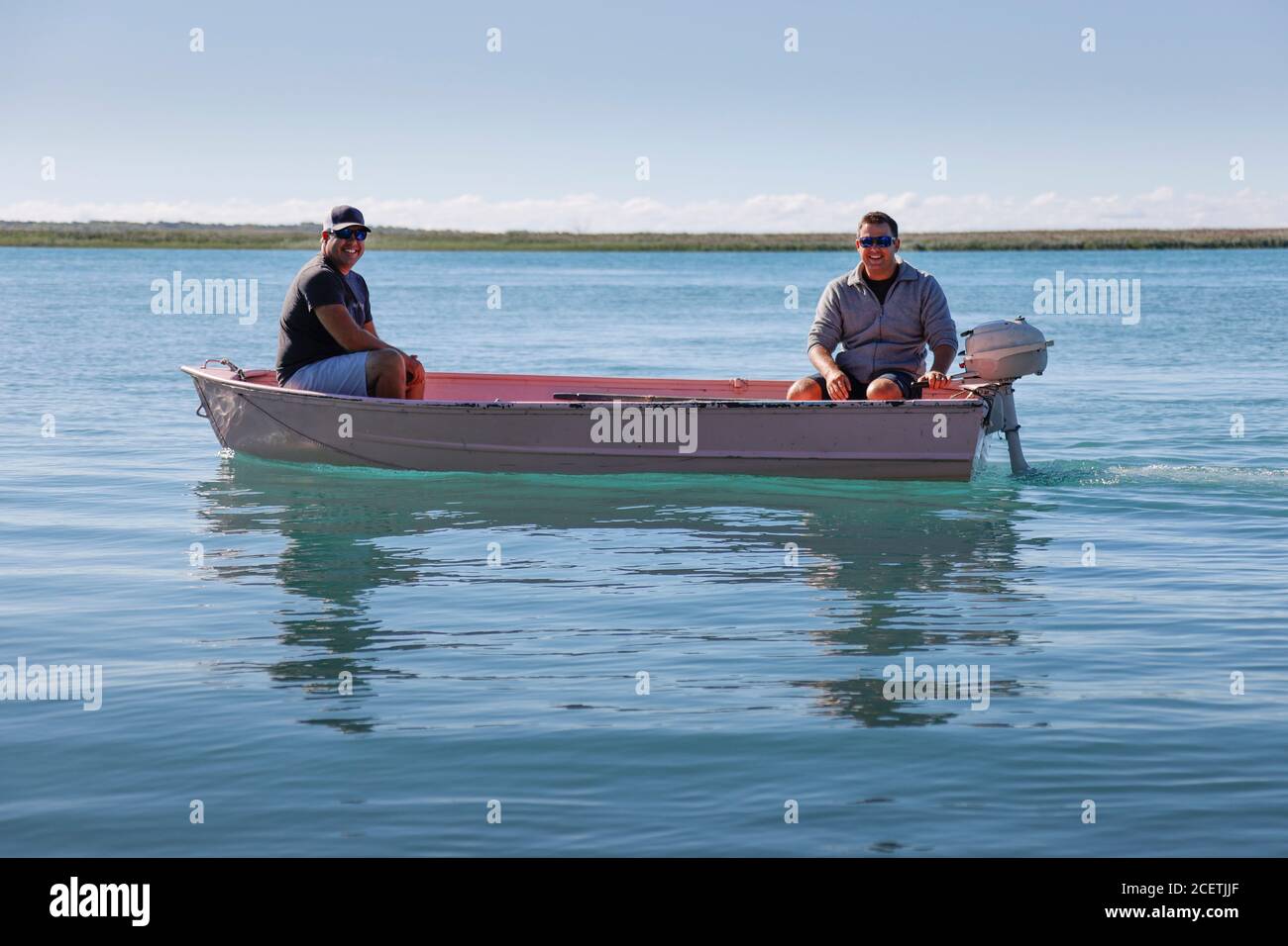 Two men driving a small outboard-powered boat on a lake. Stock Photo