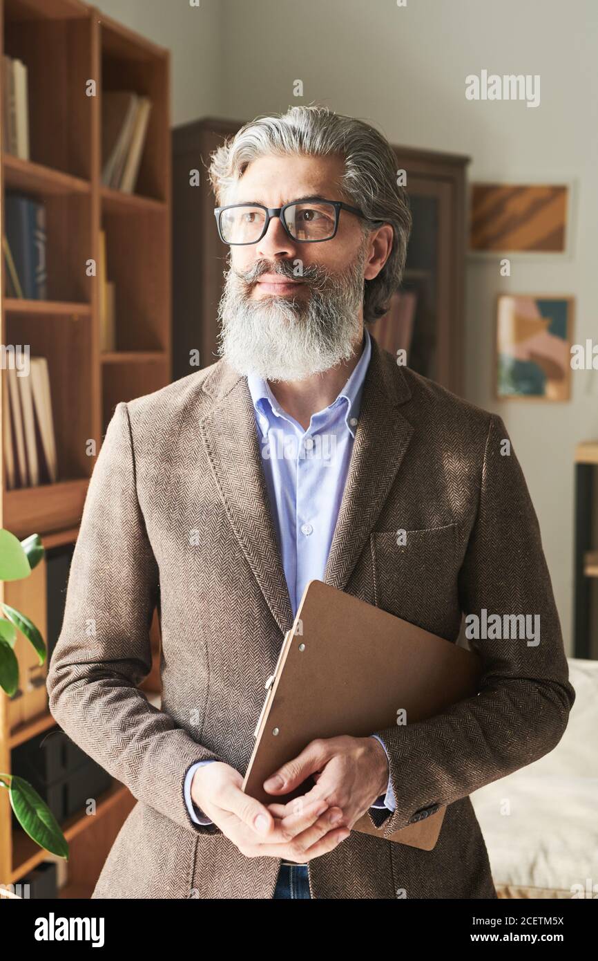 Modern mature bearded man wearing stylish outfit holding clipboard looking away, vertical medium portrait Stock Photo