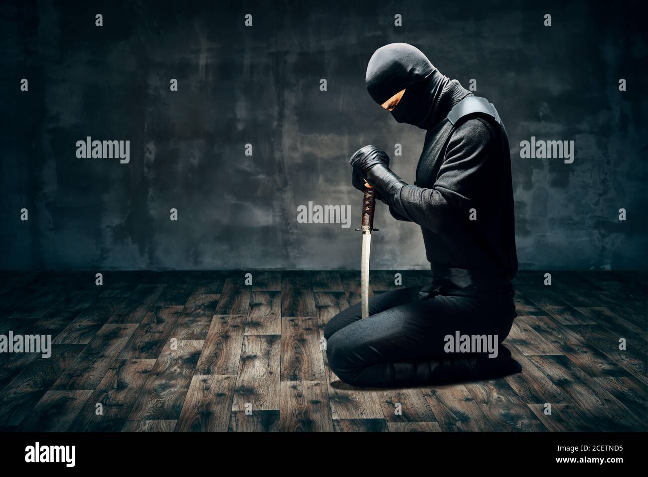 Warrior man sitting on floor posing with a sword over dark background Stock Photo