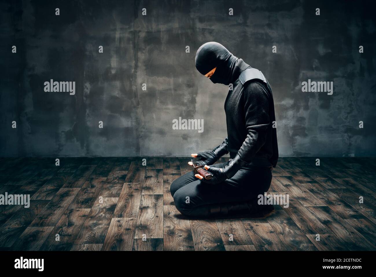 Warrior man sitting on floor posing with a sword over dark background Stock Photo