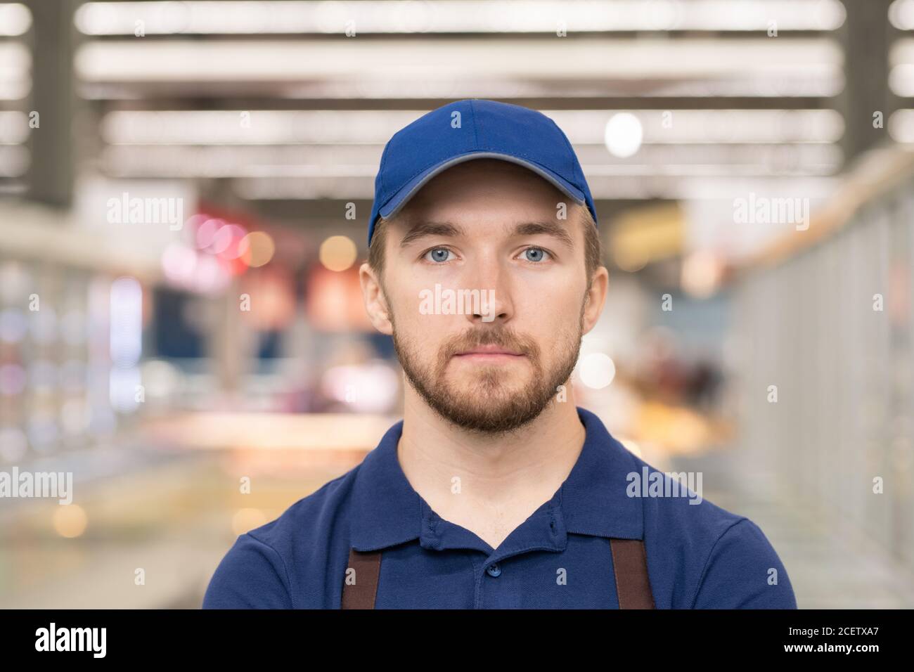 Head and shoulders portrait of handsome young man working in supermarket standing in aisle looking at camera Stock Photo