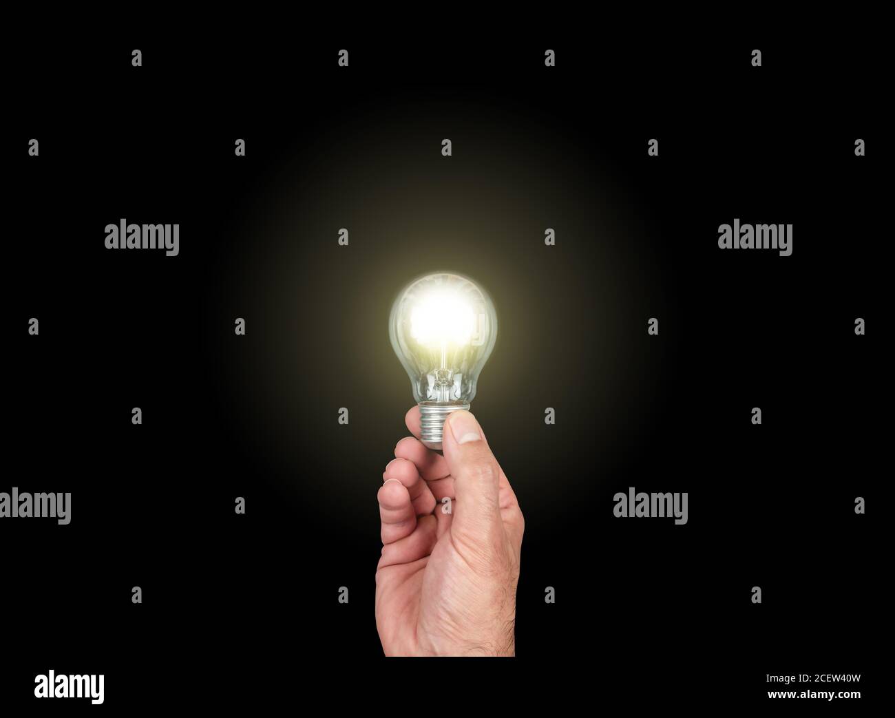 hand holding glowing light bulb against black background, having an idea concept Stock Photo