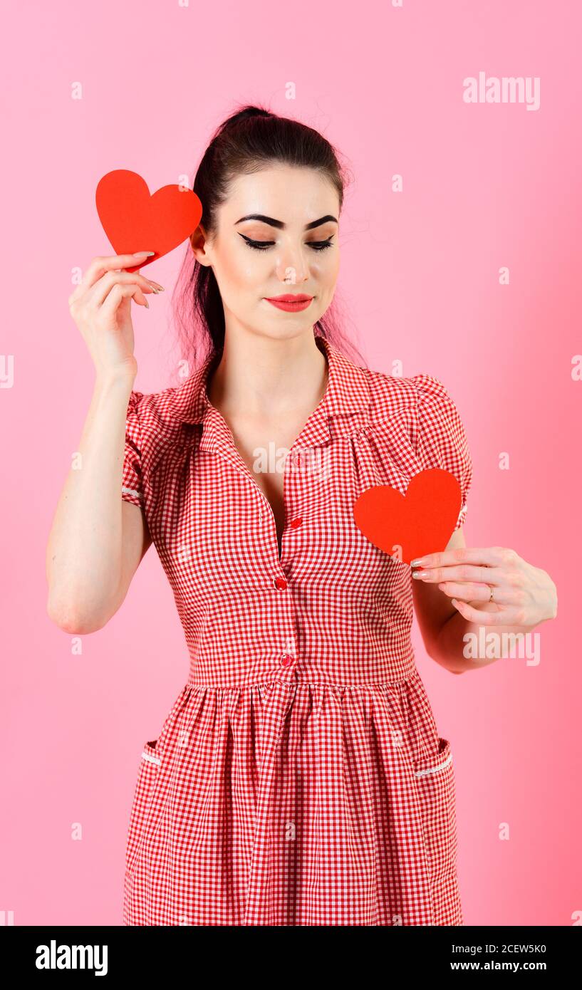 Valentines day, holiday. Girl with calm face, make up and red hearts. Woman  in stylish dress holds romantic symbols. Girl with valentine hearts  isolated on pink. Dating, relationship, beauty concept Stock Photo -
