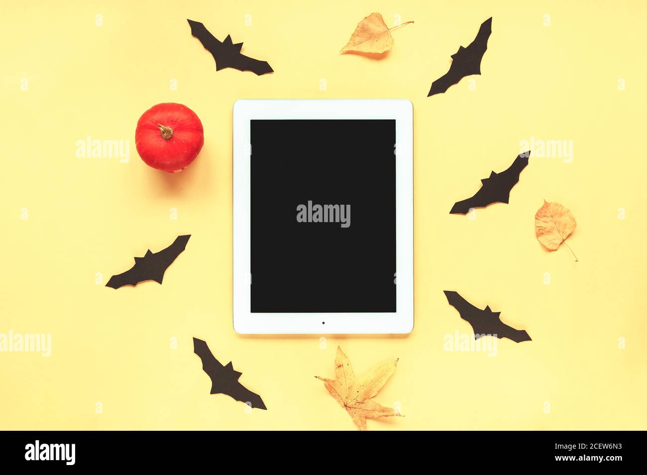 Tablet with blank screen and pumpkin, autumn leaves, handmade black bats on yellow background. Halloween concept. Top view, flat lay. Stock Photo