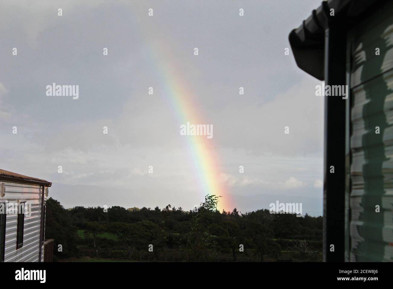 End of a rainbow into the countryside in a dark sky in Pwllheli, North Wales Stock Photo