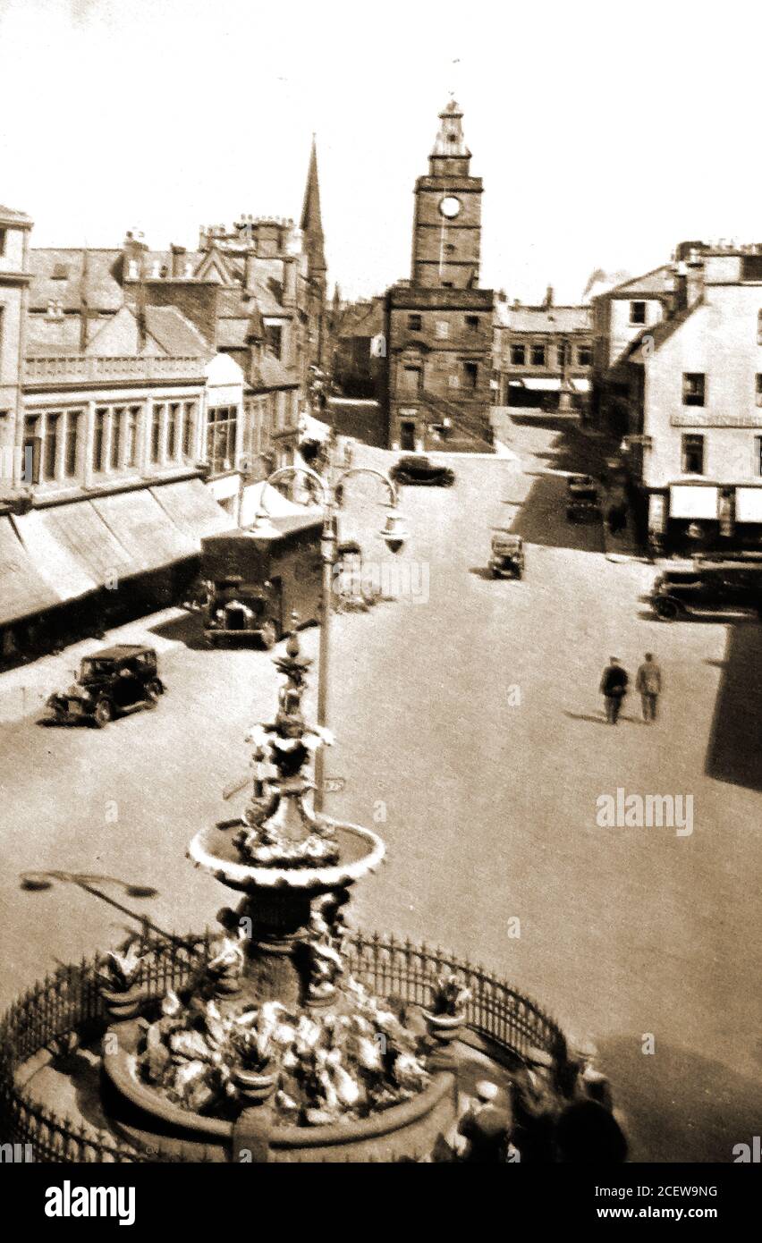 A 1933 book illustration showing Dumfries City Centre, Scotland featuring old motor vehicles, midsteeple clock tower  shops with sun blinds  & the central fountain in the High Street. Residents are known locally as Doonhamers. The towns 1st fountain was unveiled on the 5th of December 1882 by  the Provost to commemorate the supply of public drinking water to the town from nearby Lochrutton following many cases of cholera killing local residents from a previously bad water supply.  It was made by the Sun Foundry, Alloa, and is one of only two models of its type known anywhere in the world. Stock Photo
