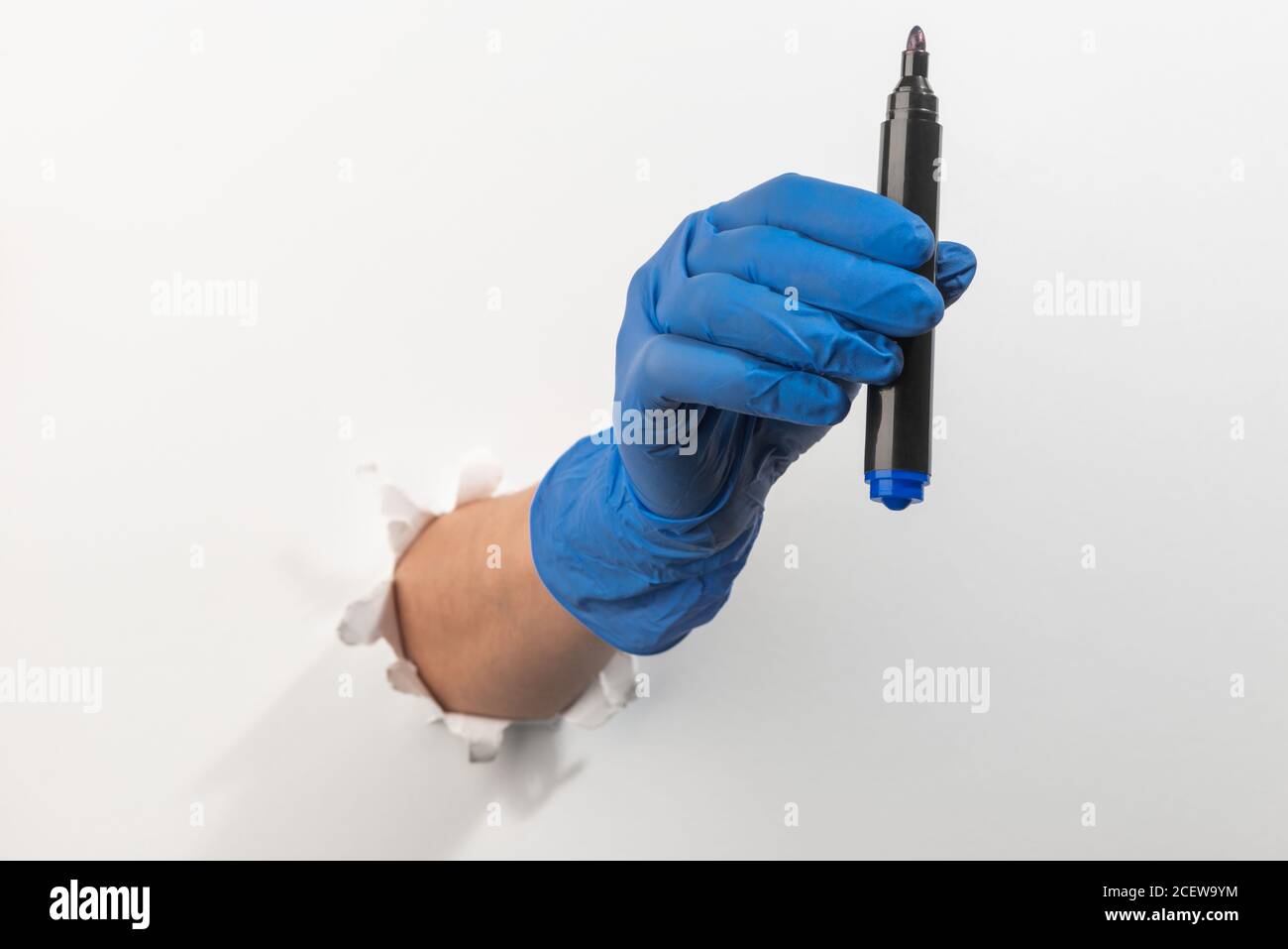 Hand in a latex glove giving a permanent marker through torn white wall