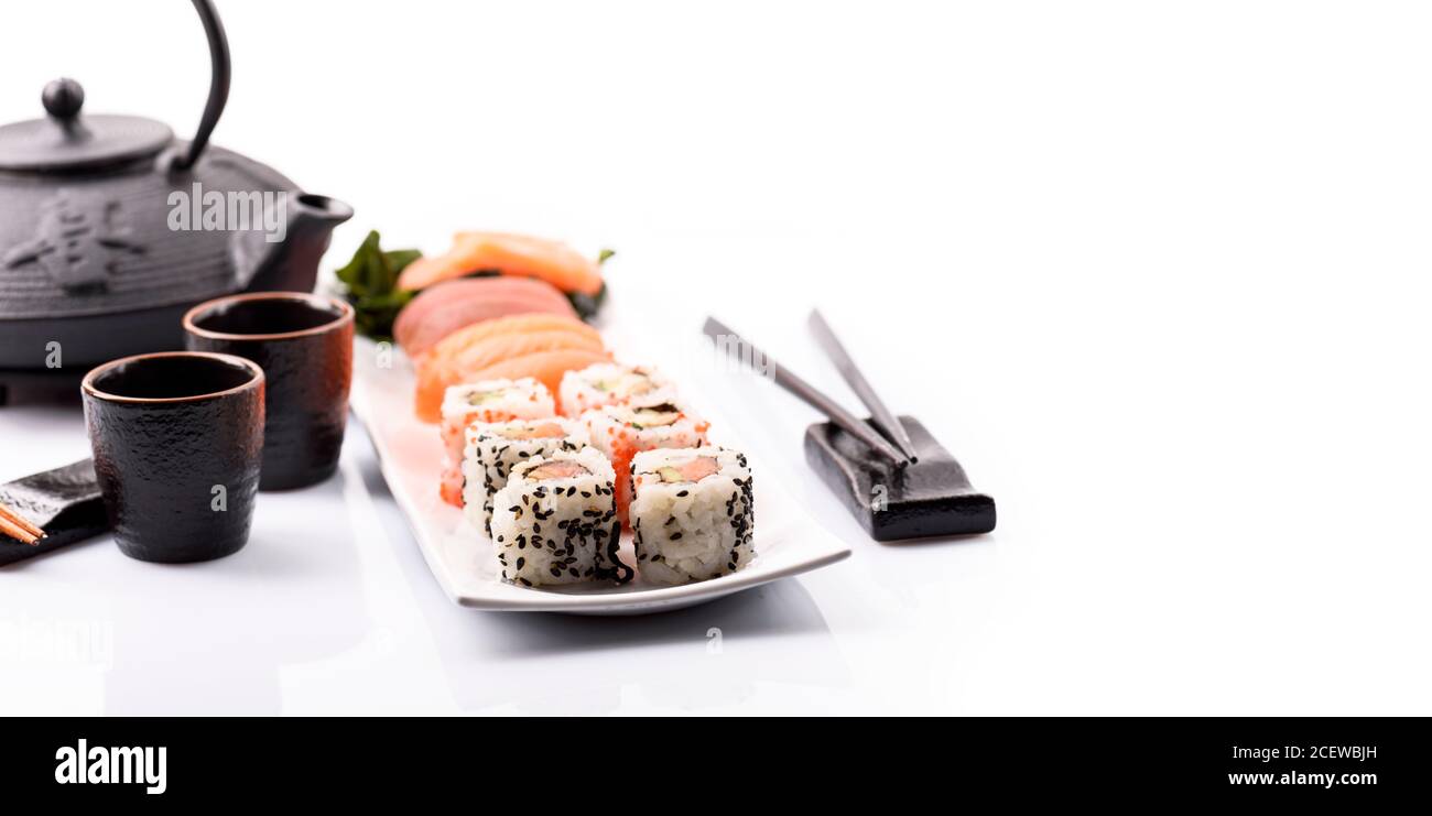 Closeup of sushi roll dish with bamboo chopstick frame isolated on white background. Luxury japanese restaurant dinner with sashimi, maki, surimi, tea Stock Photo