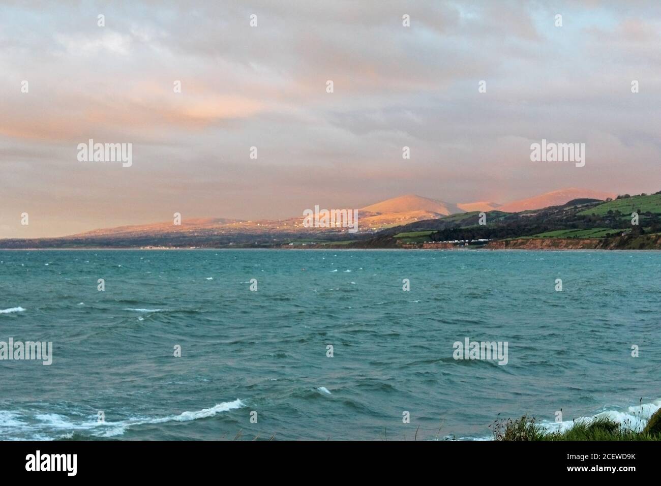 Sunset lit mountains and town in the distance over the Irish Sea at Trefor, North Wales Stock Photo