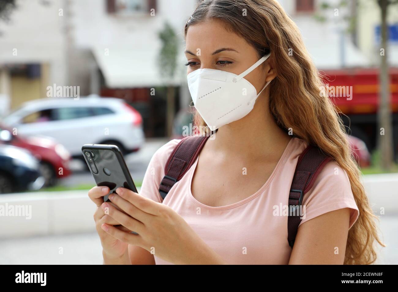 Close up of student female with protective mask messaging with smart phone in city street Stock Photo