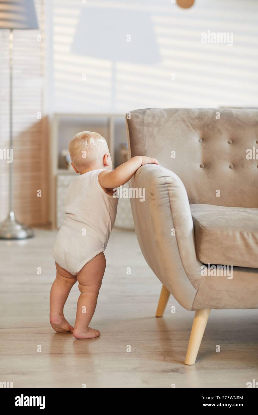 Vertical back view shot of unrecognizable toddler holding on sofa learning how to stand on his legs, copy space Stock Photo