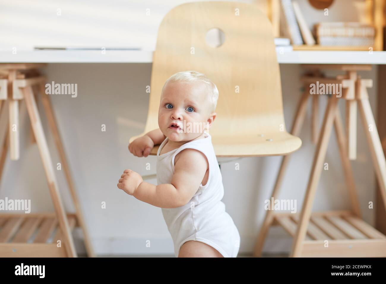 Caucasian toddler boy holding on chair learning how to stand on his legs copy space Stock Photo
