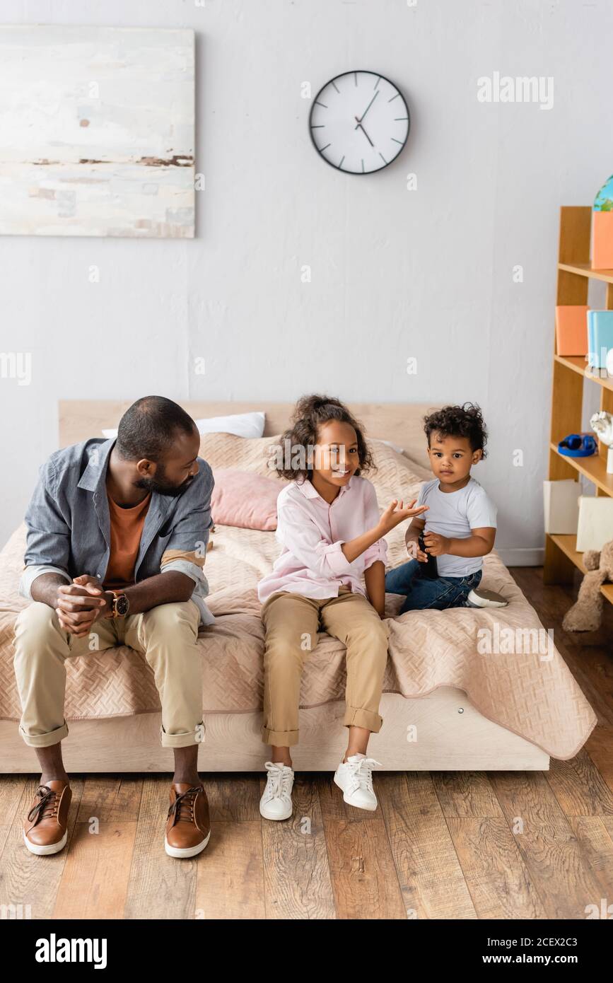 young african american father and children in casual clothes sitting on bed at home Stock Photo