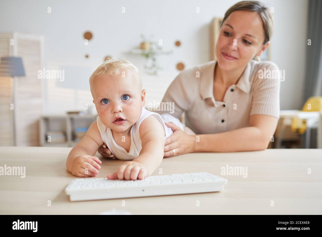 Funny little baby trying to play with computer keyboard while his mother holding him, horizontal shot, copy space Stock Photo