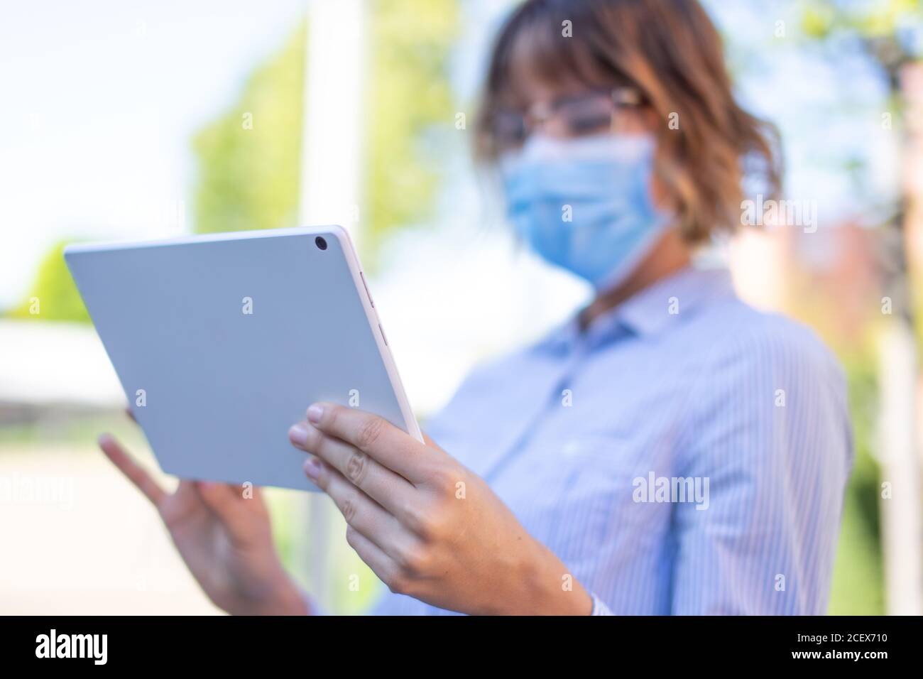 Young businesswoman in mask using digital tablet in park, depth of field Stock Photo