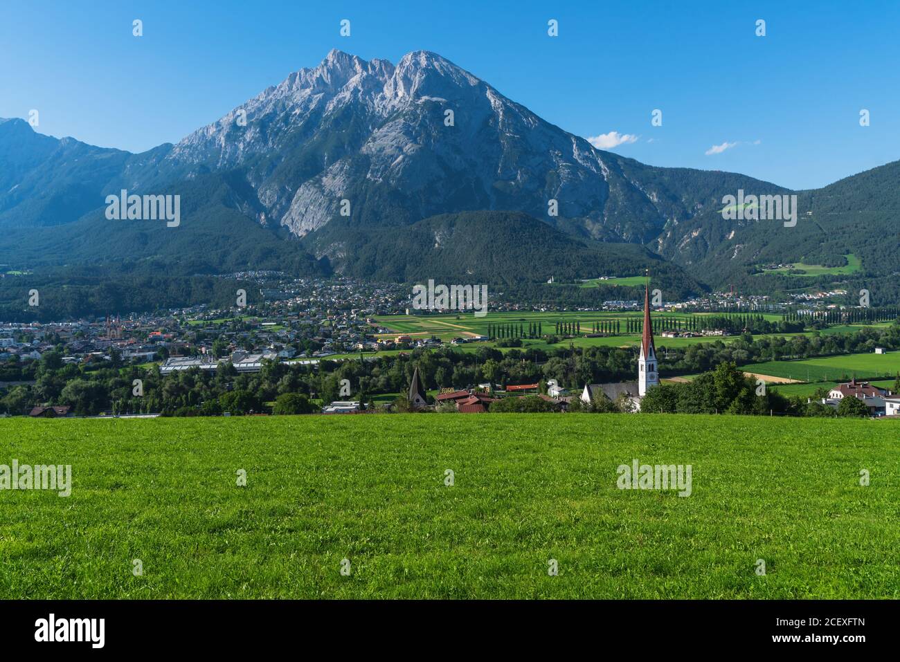 Panoramic view over sunny meadow on summer valley with villages and city with alpine rocky mountain range background, Pfaffenhofen, Telfs, Tirol, Aust Stock Photo