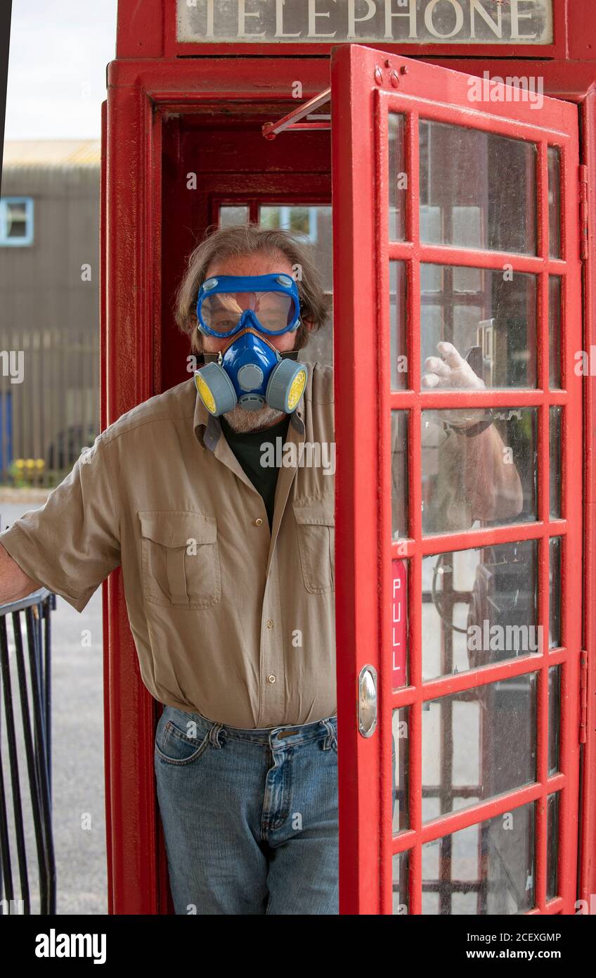 Hampshire, England, UK. 2020. Man exiting a red public phone box wearing a mask and goggles during Covid-19. Stock Photo