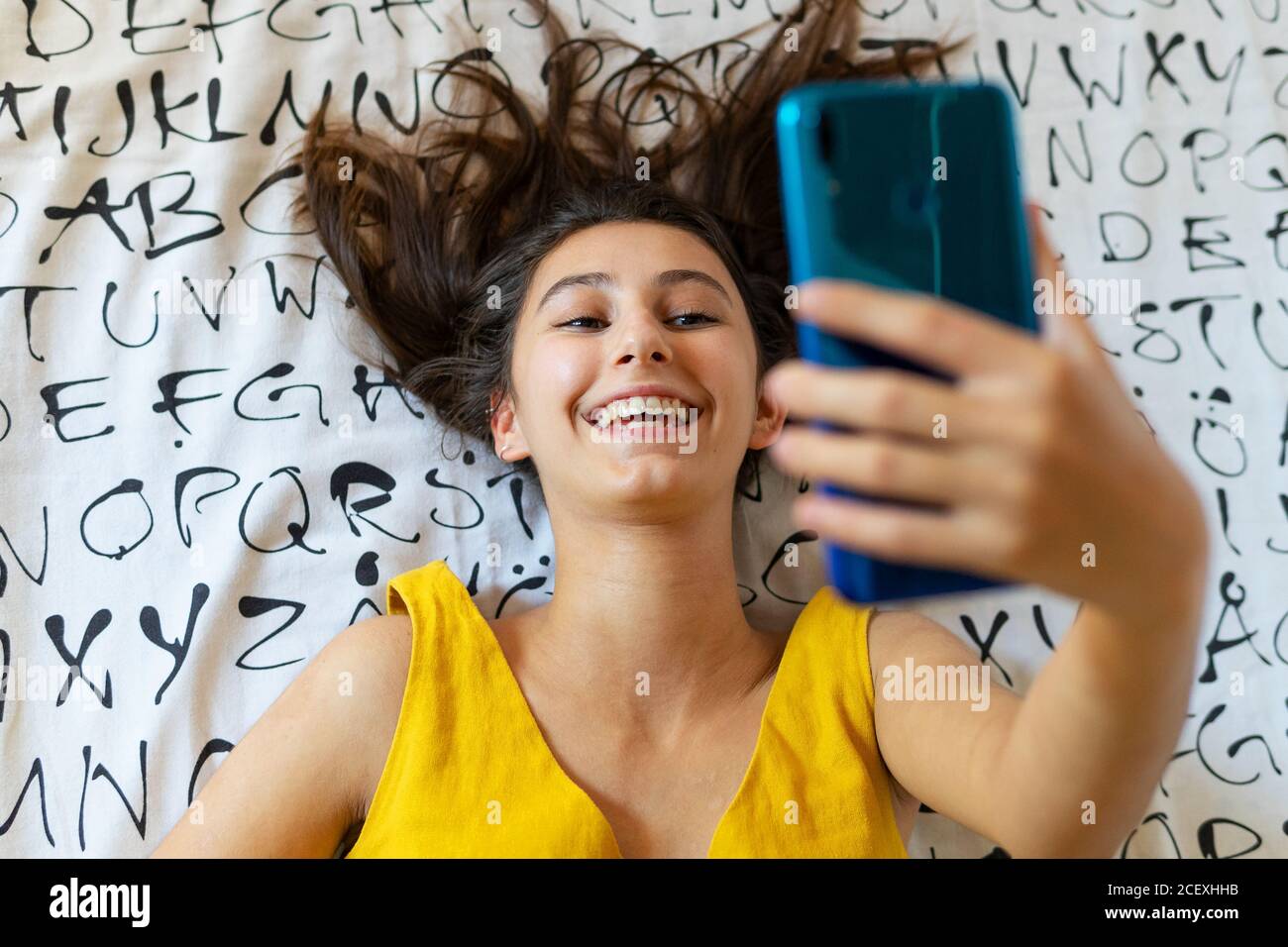 High angle of delighted female lying on bed and taking photo on selfie camera while entertaining during weekend at home Stock Photo
