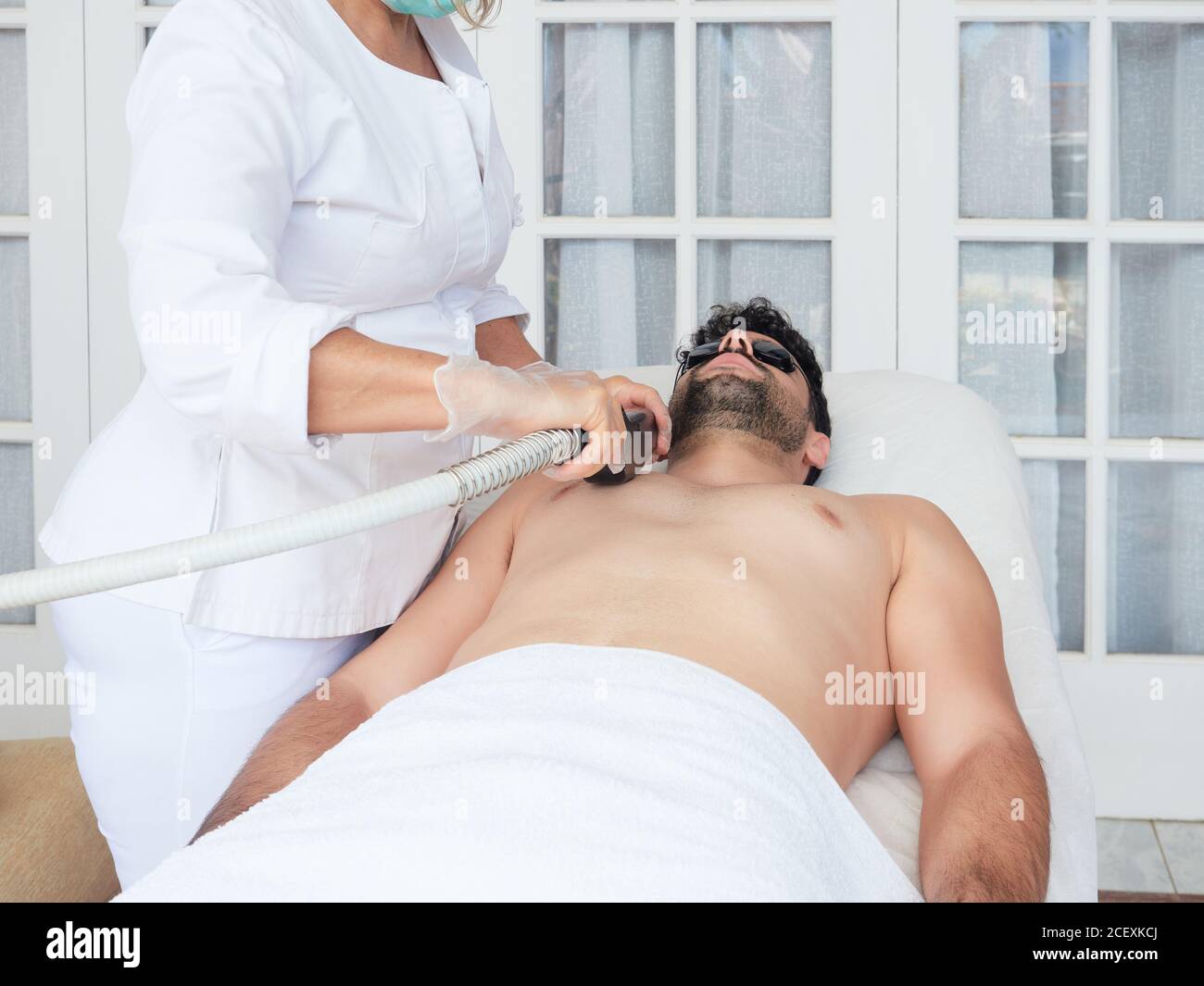 Cropped faceless master using laser apparatus on male face removing beard face during procedure in salon Stock Photo