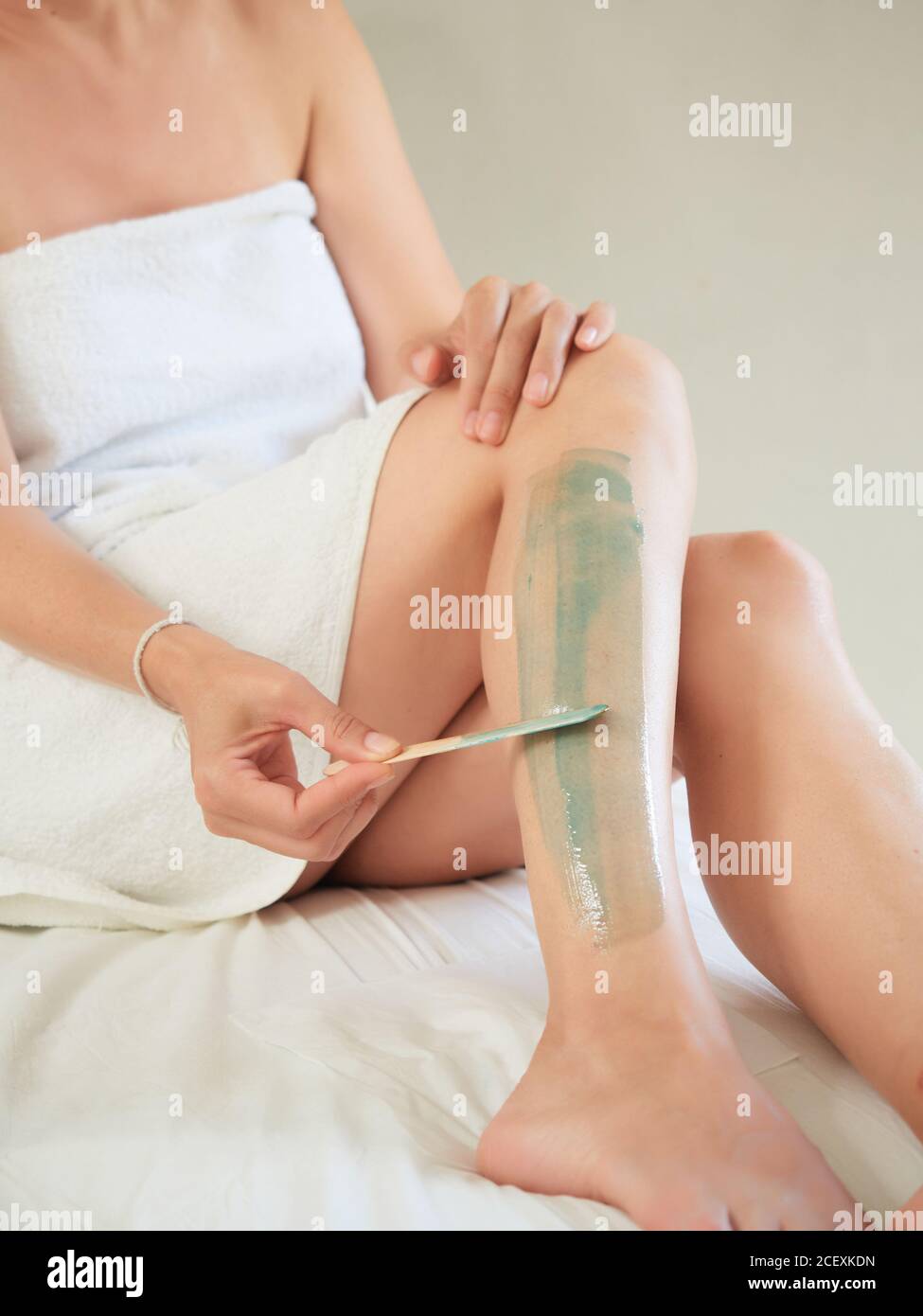 Cropped unrecognizable female removing leg hair in bathrobe using hot wax in salon Stock Photo