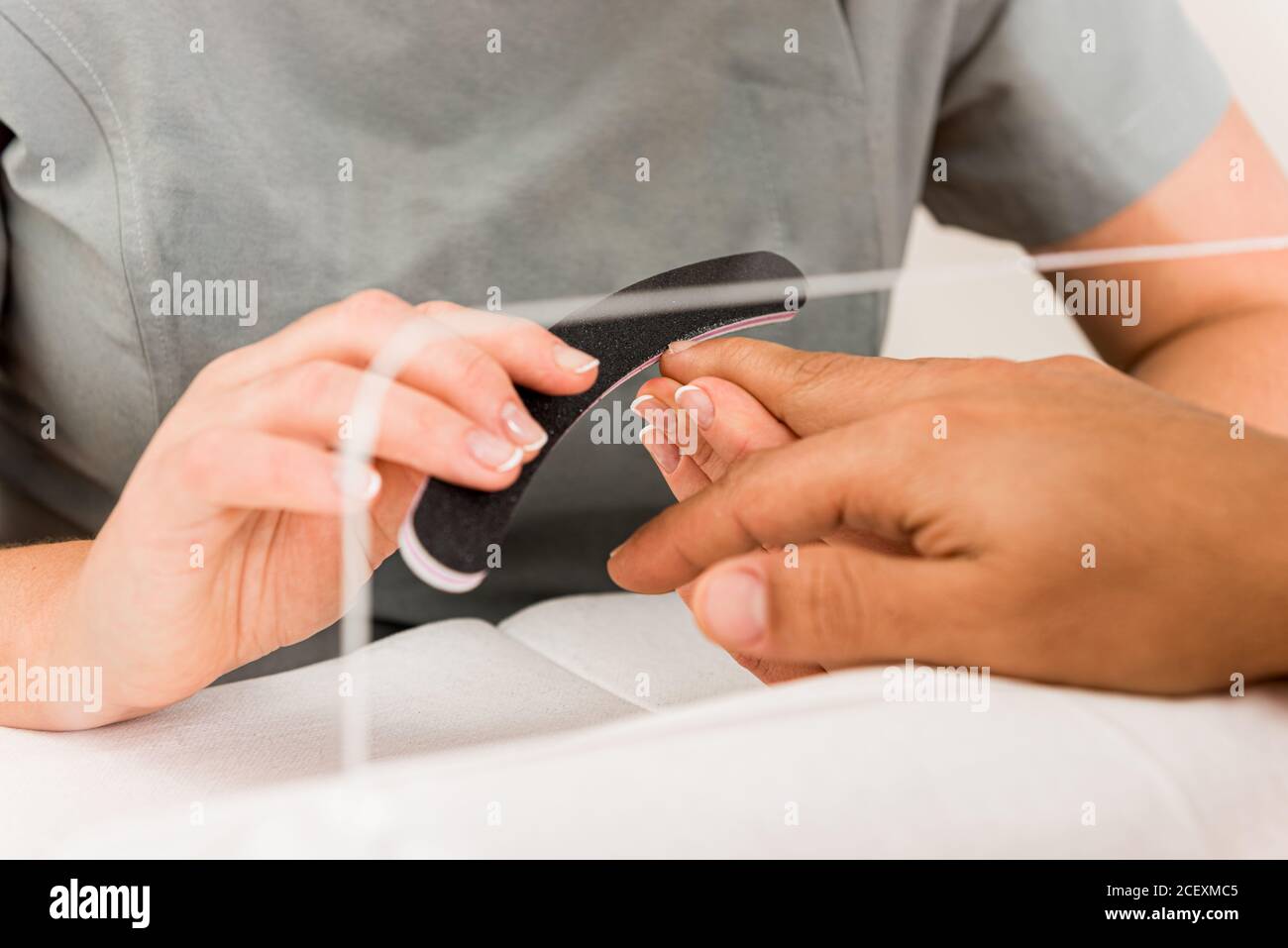 Cropped unrecognizable female specialist doing professional manicure procedure in cropped anonymous male in modern beauty center Stock Photo