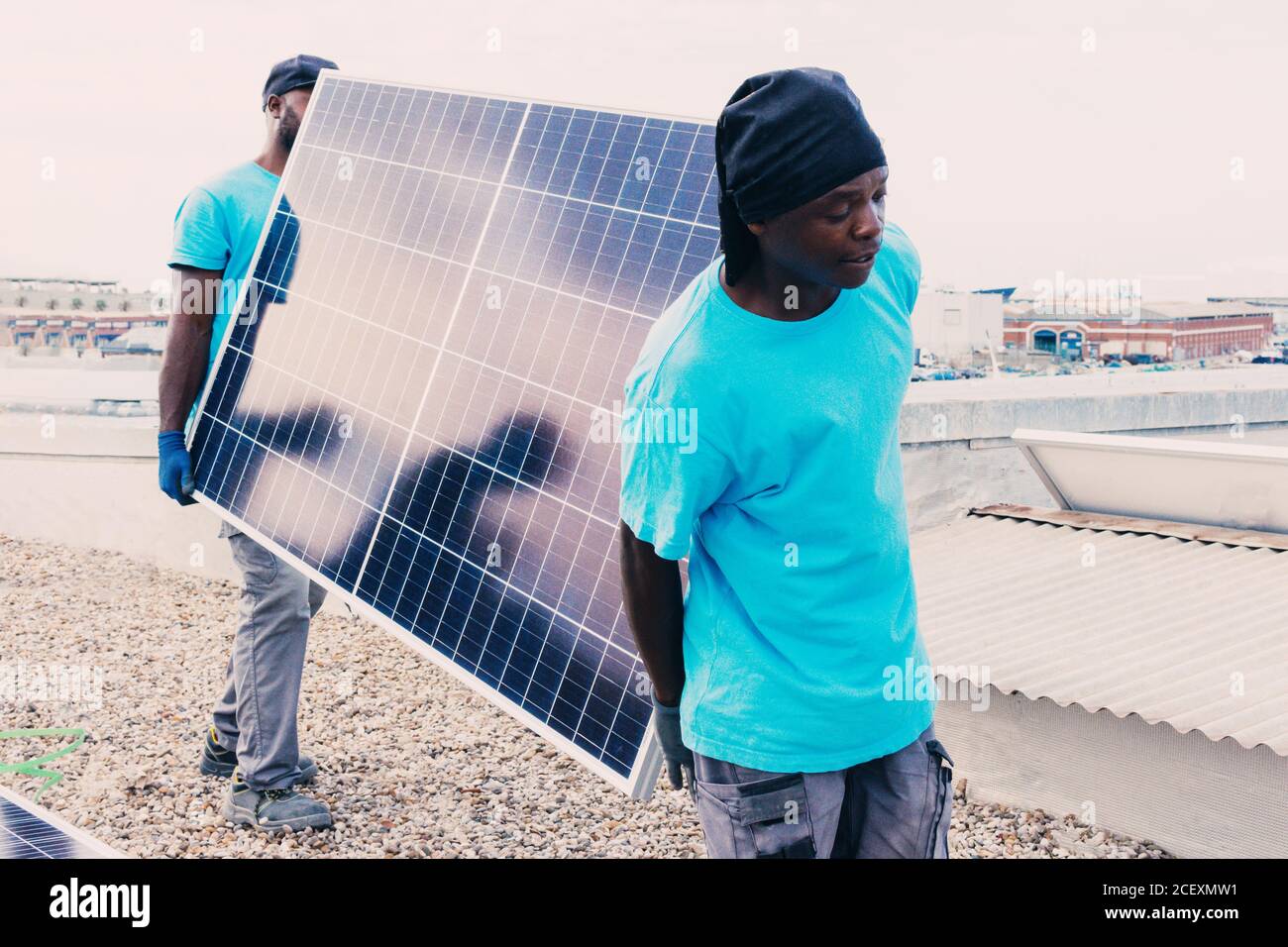 African American workers walking with solar panel on sunny day in industrial area Stock Photo