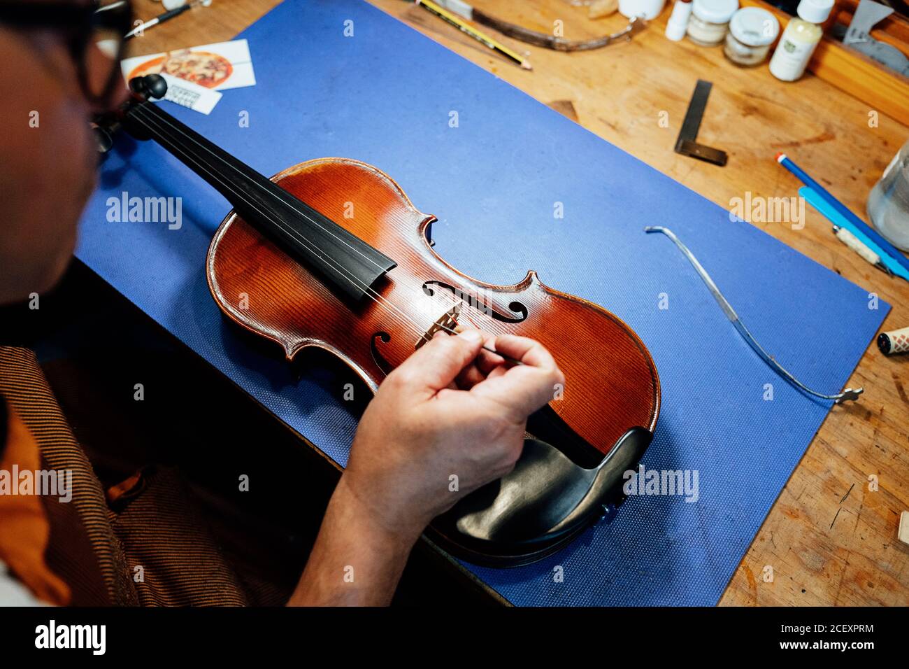 Crop unrecognizable male artisan master setting bridge on violin after