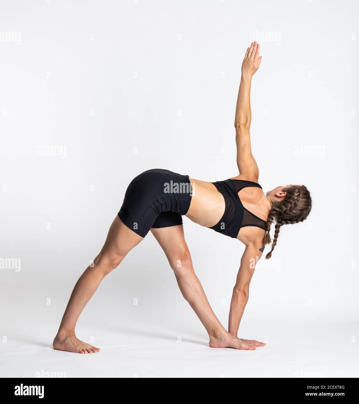 Full body side view of young barefoot female in sportswear performing Revolved Triangle yoga pose against white background Stock Photo