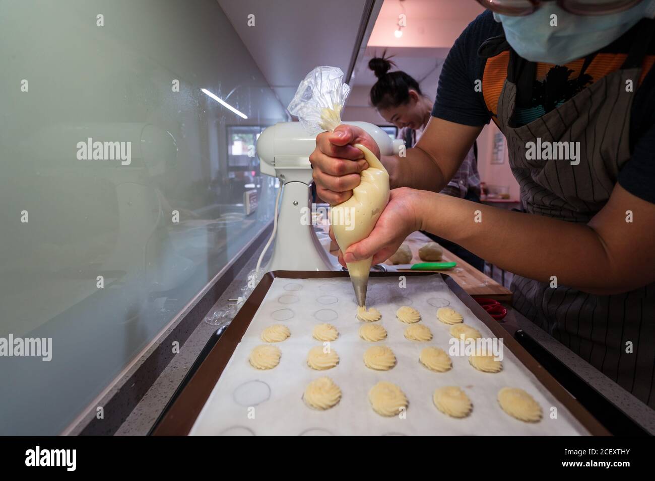 https://c8.alamy.com/comp/2CEXTHY/anonymous-person-with-pastry-bag-piping-cookie-batter-on-baking-pan-at-wooden-table-2CEXTHY.jpg