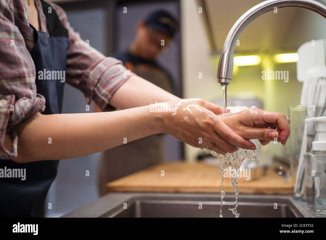 Cropped side view of Woman washing hands in sink while having home bakery with man Stock Photo