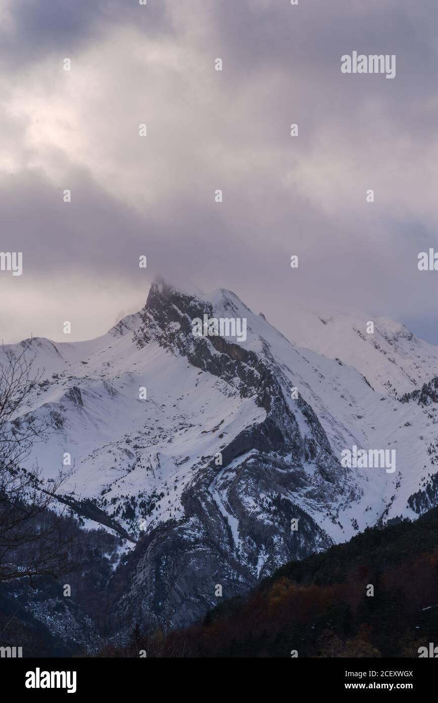 Sharp mountain peaks covered partially with snow under picturesque cloudy sky in wintertime Stock Photo