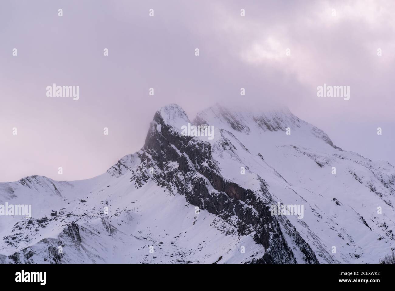 Sharp mountain peaks covered partially with snow under picturesque cloudy sky in wintertime Stock Photo