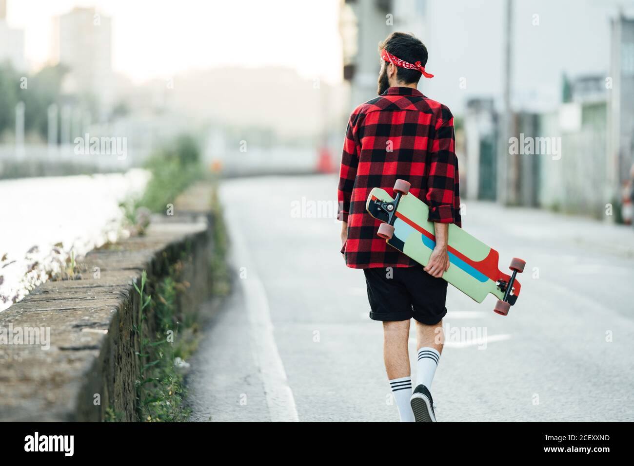 Back view of male skater in checkered shirt and with longboard walking  along asphalt road while relaxing during summer weekend in city Stock Photo  - Alamy