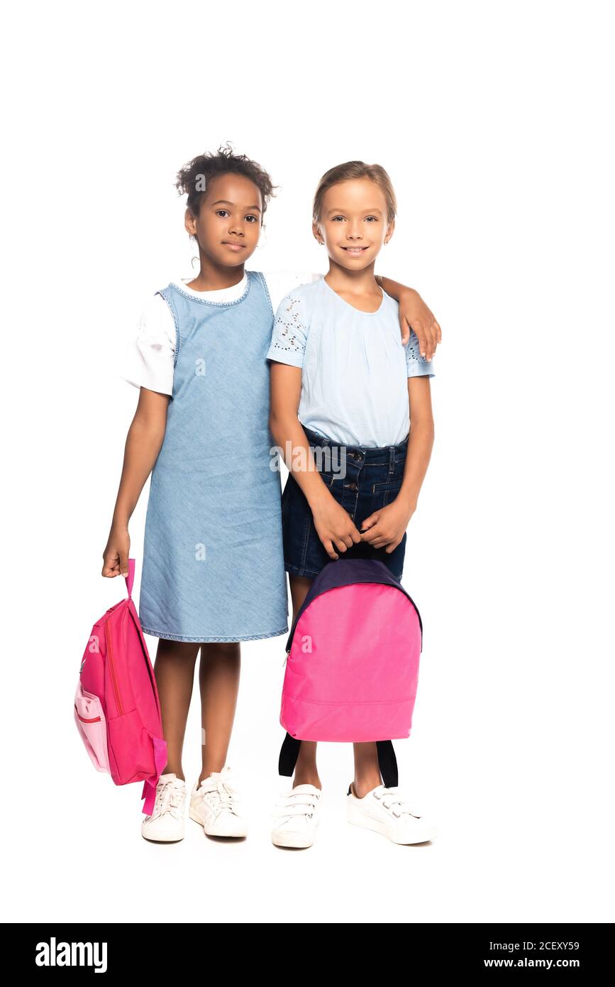 multicultural schoolgirls holding backpacks while hugging isolated on white Stock Photo