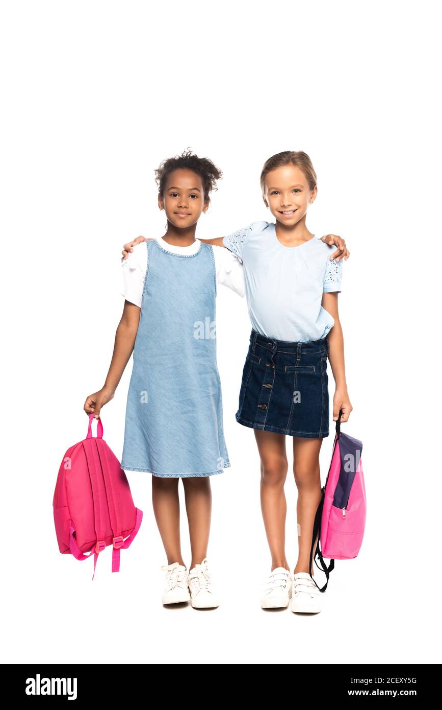 multicultural schoolgirls holding backpacks and hugging isolated on white Stock Photo