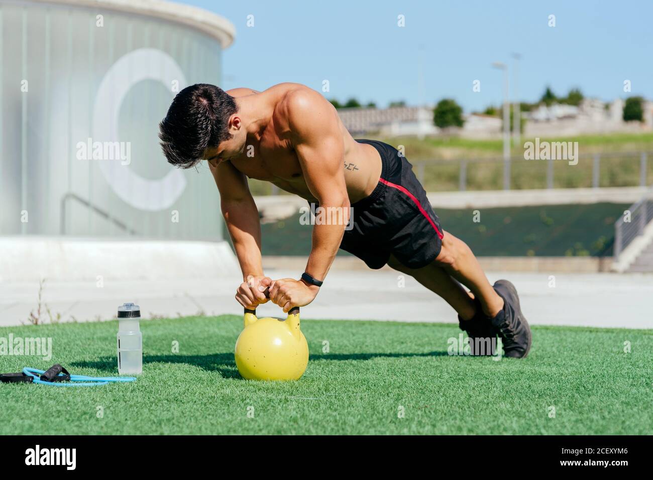 Side view of shirtless male athlete doing push ups from kettlebell during  training on lawn on summer day Stock Photo - Alamy