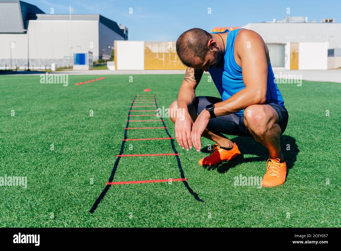 Full body exhausted male athlete sitting near agility ladder after intense workout at stadium in