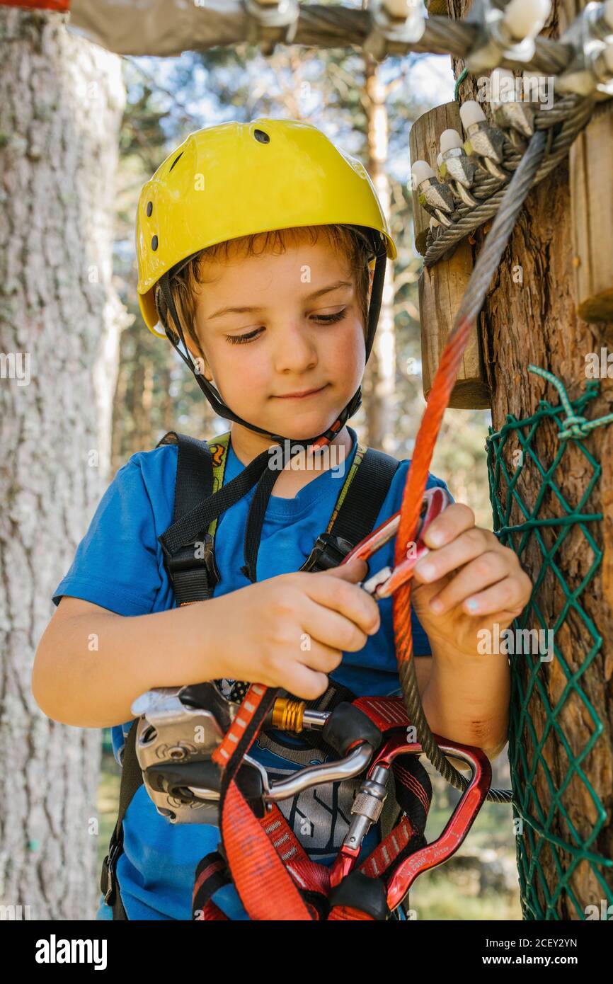 Adorable child in protective helmet and safety harness putting carabine